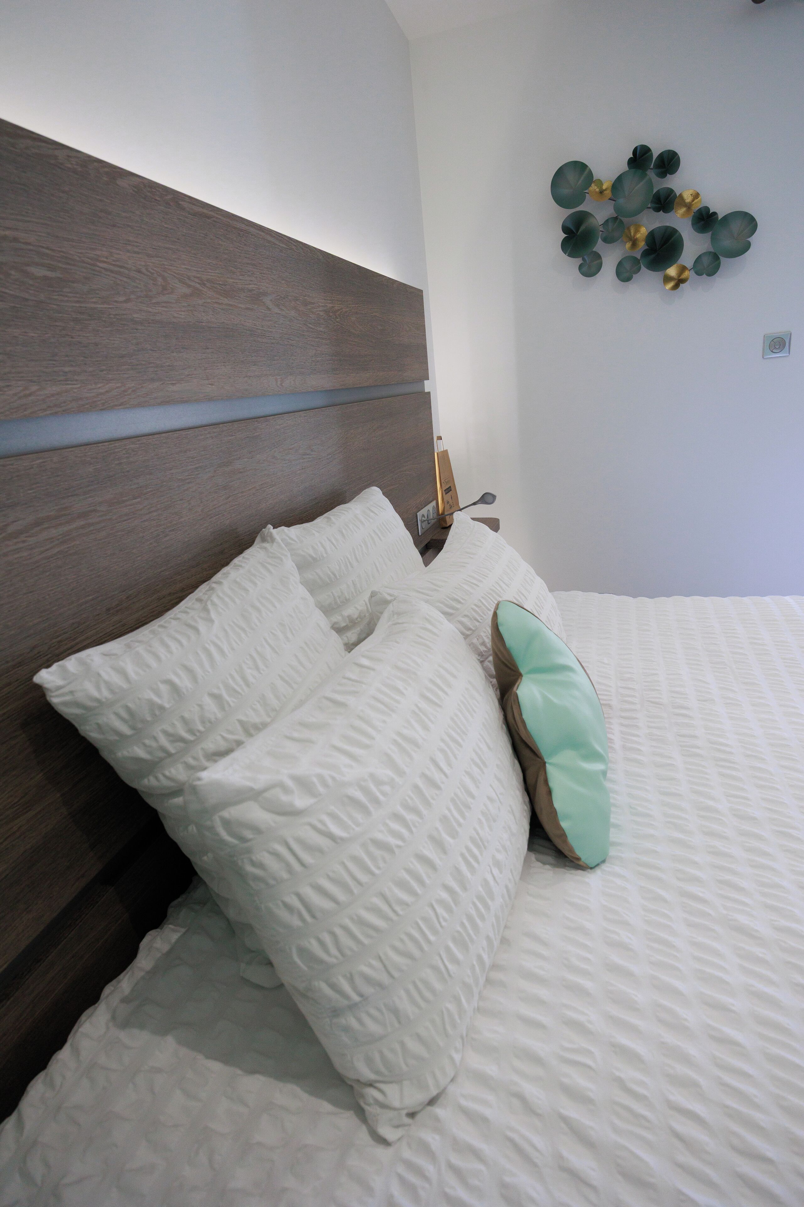 A neatly made bed with white and teal pillows, a wooden headboard, and a wall-mounted decorative piece.