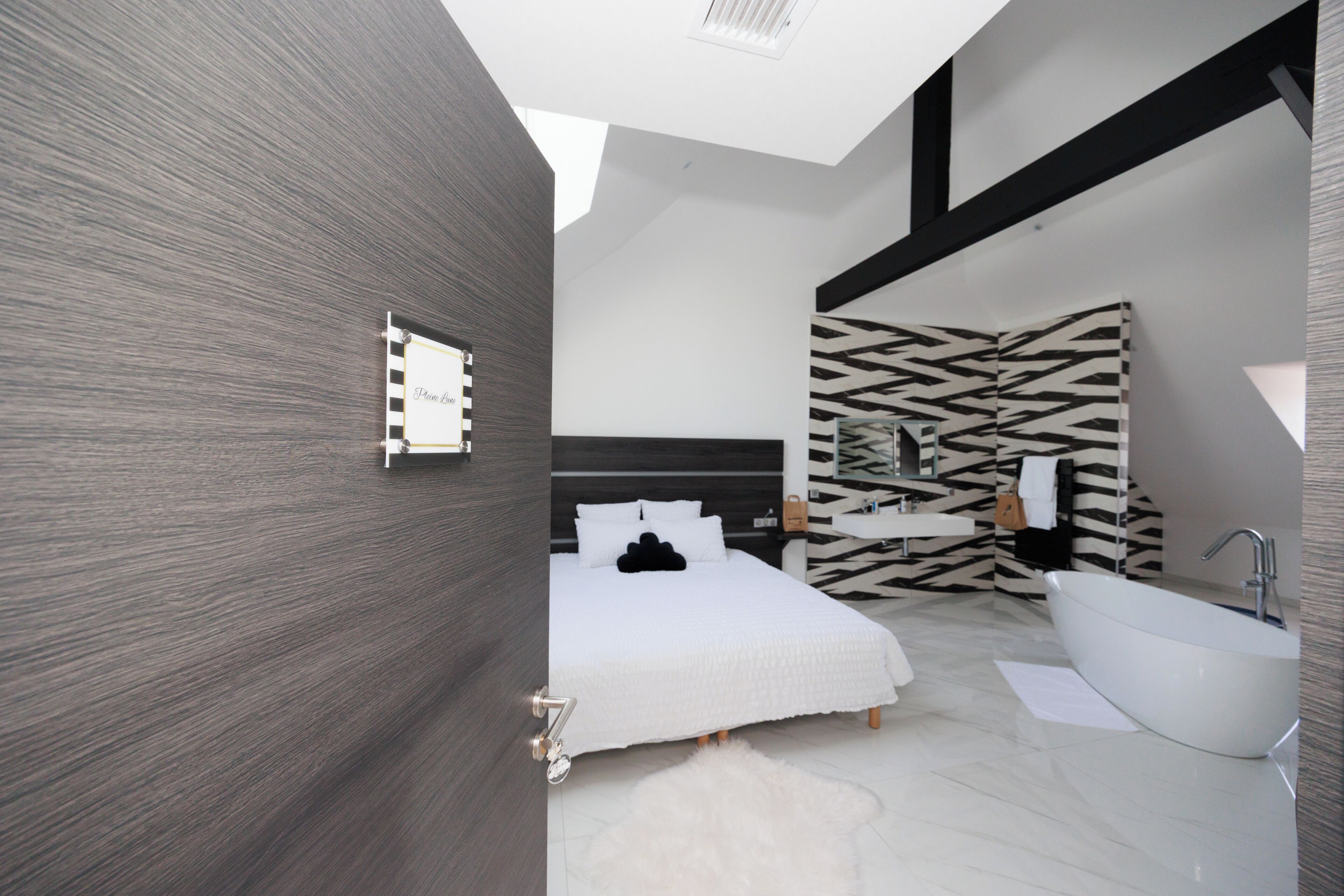 A modern bedroom with a large bed, a white bathtub, and a zebra-patterned wall.