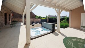 Un patio couvert avec un jacuzzi, des sièges d’extérieur et une vue sur la campagne.