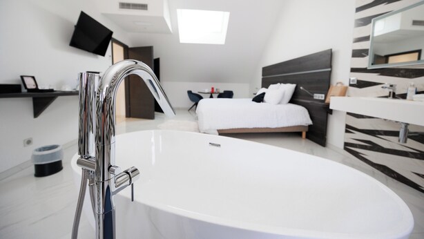 Une salle de bain moderne avec une grande baignoire blanche, une douche à jets élégants et un téléviseur fixé au mur, au-dessus du lit.