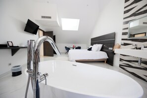 A modern bathroom with a large white bathtub, a sleek showerhead, and a mounted television above the bed. - Les Chambres d'à Côté - Le Saisonnier (Roye)
