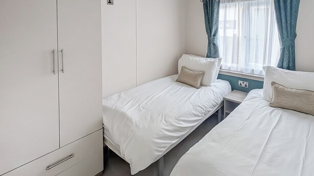 Une chambre avec deux lits simples, une armoire, une fenêtre avec des rideaux et une table de chevet.