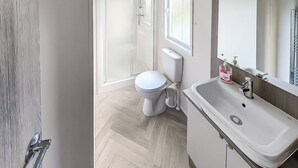 Une salle de bain moderne avec un sol en parquet point de Hongrie, des toilettes blanches, un lavabo avec un miroir et une porte dotée d’une poignée.