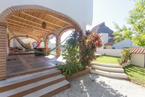 Un patio con una hamaca, escalones que llevan a una zona cubierta y plantas en macetas.