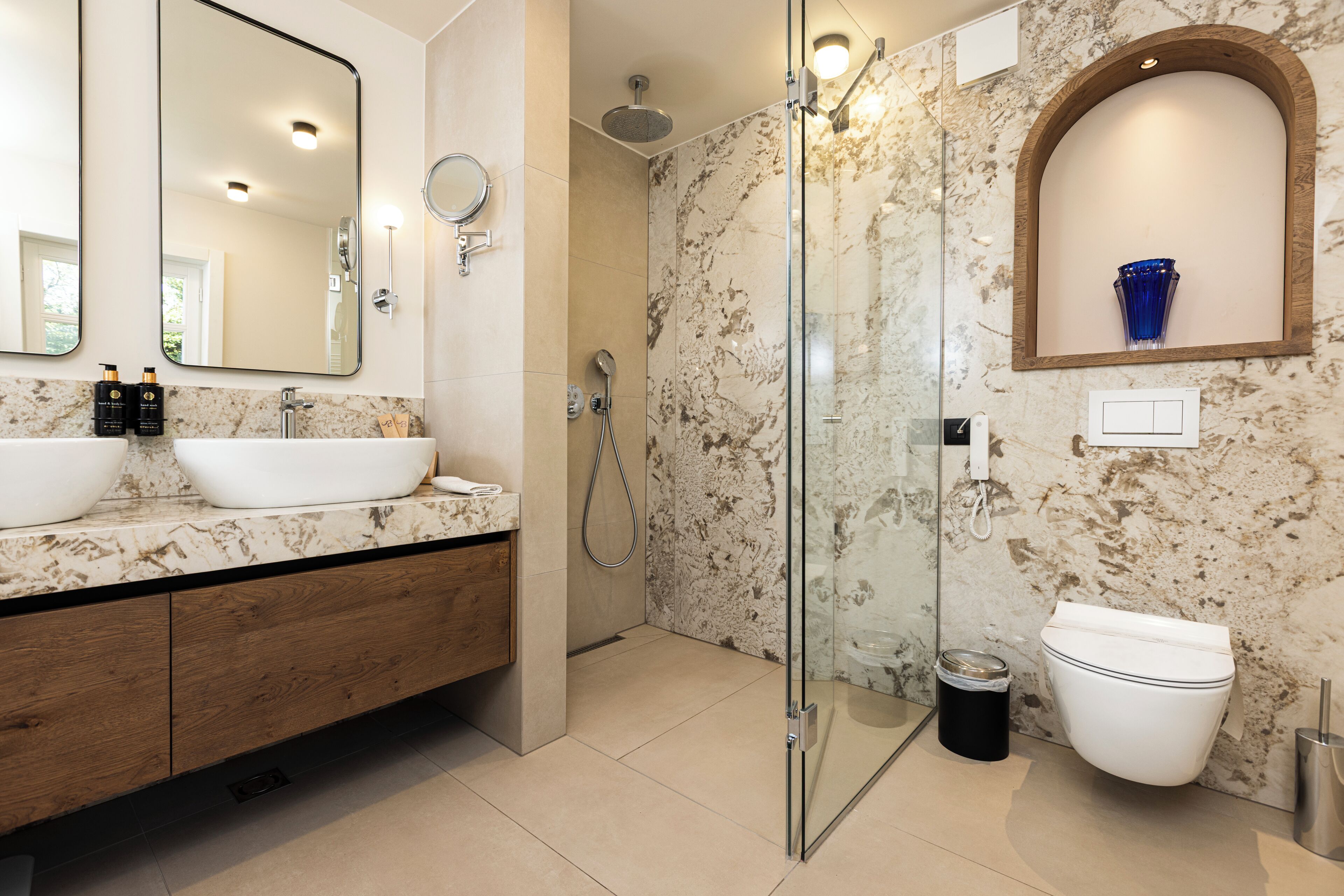 A modern bathroom with a marble vanity, a glass-enclosed shower, and a white toilet.