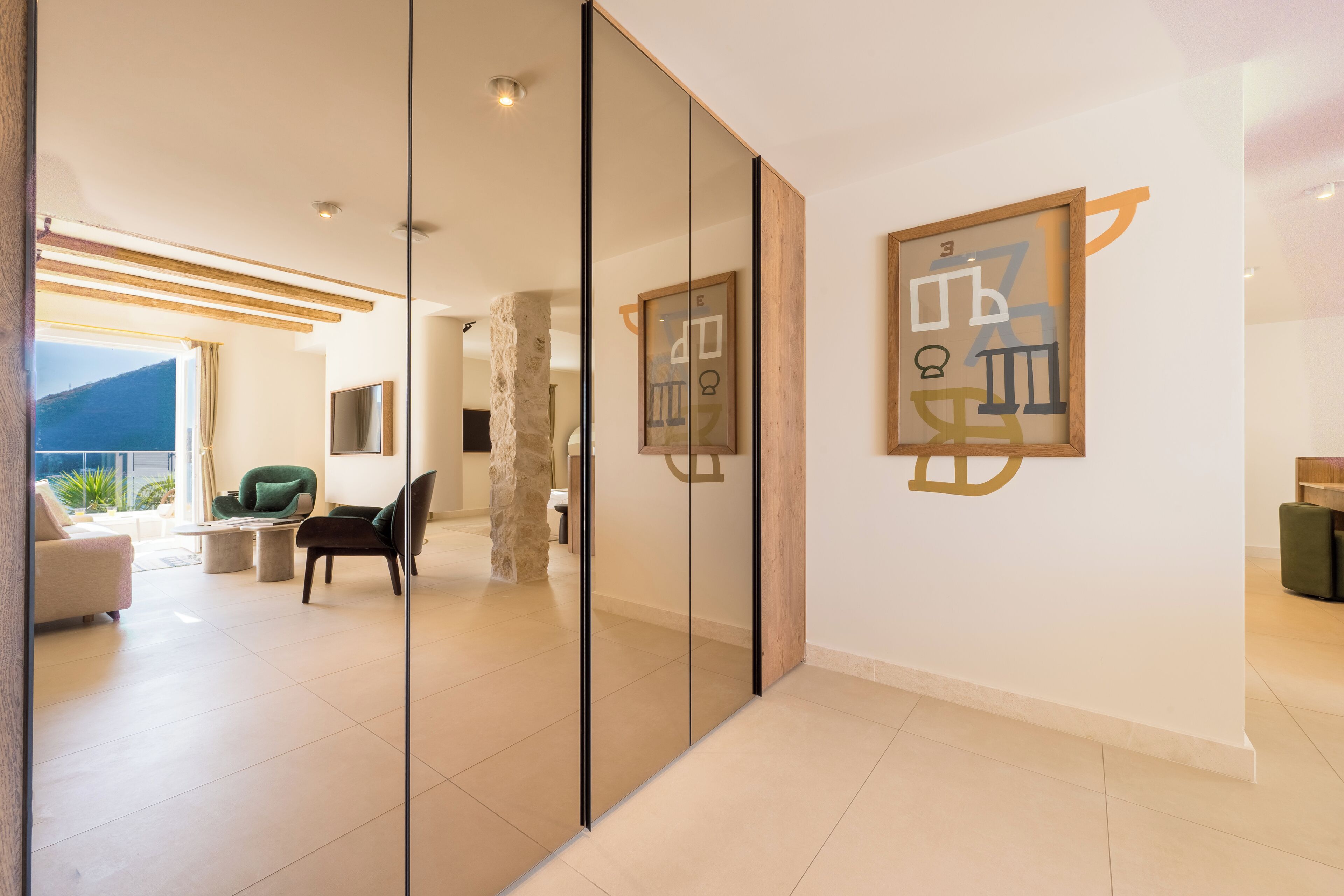 Un interior moderno con un separador de vidrio, un pilar de piedra, una silla verde y una obra de arte enmarcada en la pared.