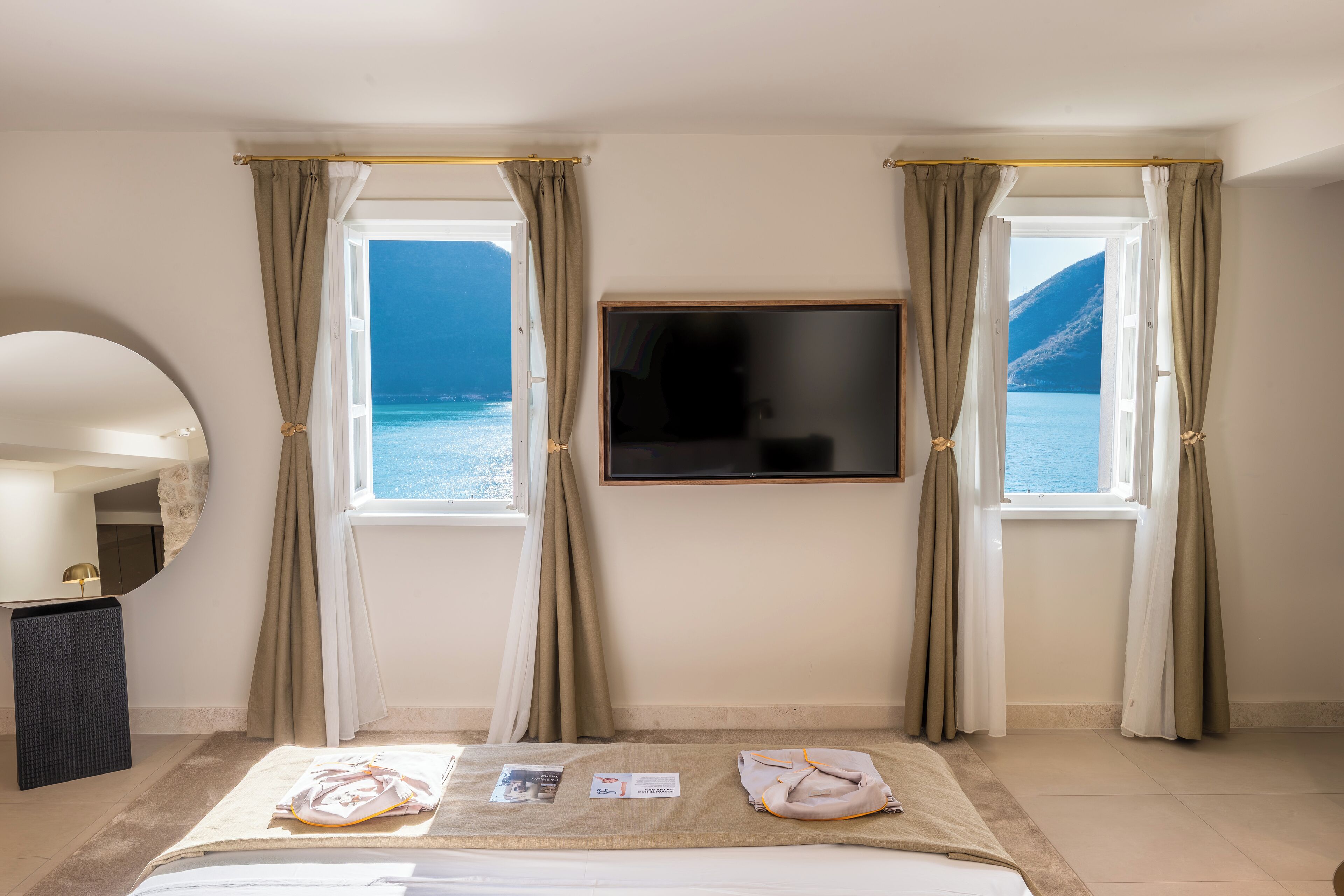 A hotel room with a bed, a TV mounted on the wall, and two windows with curtains.