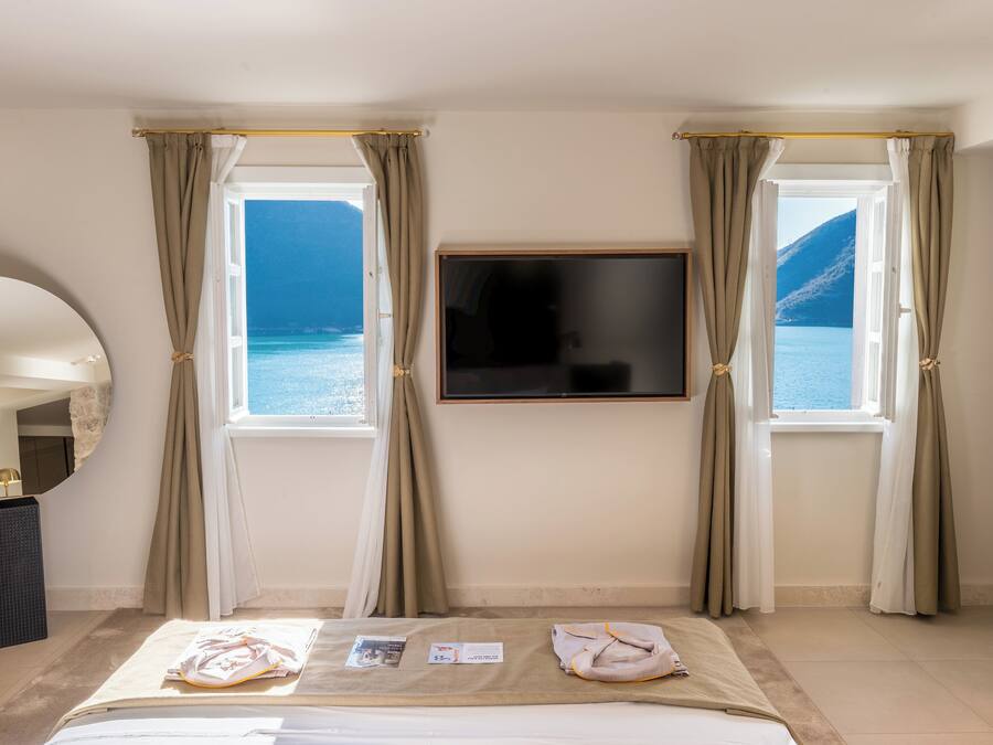 A hotel room with a bed, a TV mounted on the wall, and two windows with curtains.