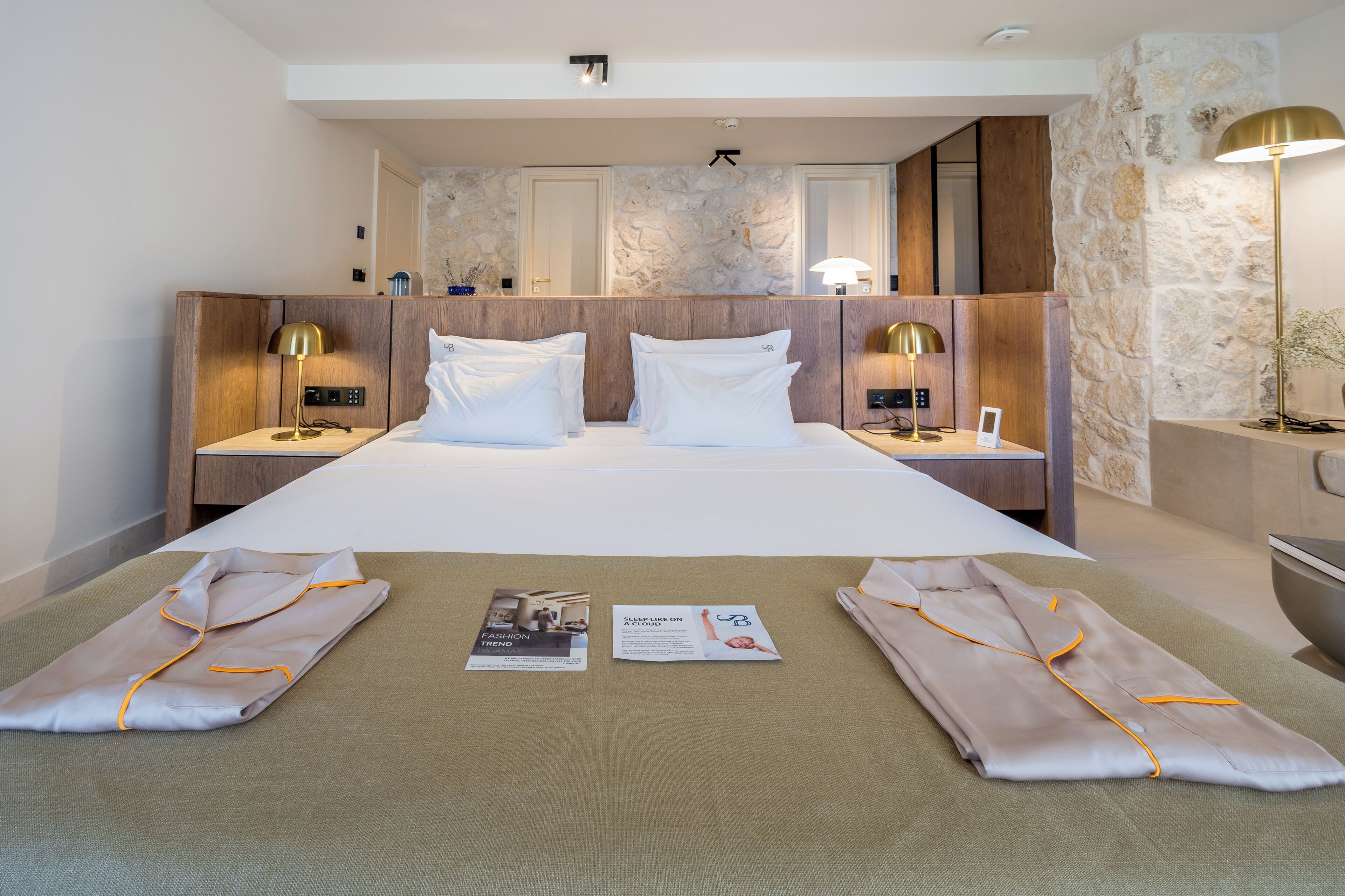 A hotel room with a large bed, two bedside tables with lamps, a stone accent wall, and a mirror.