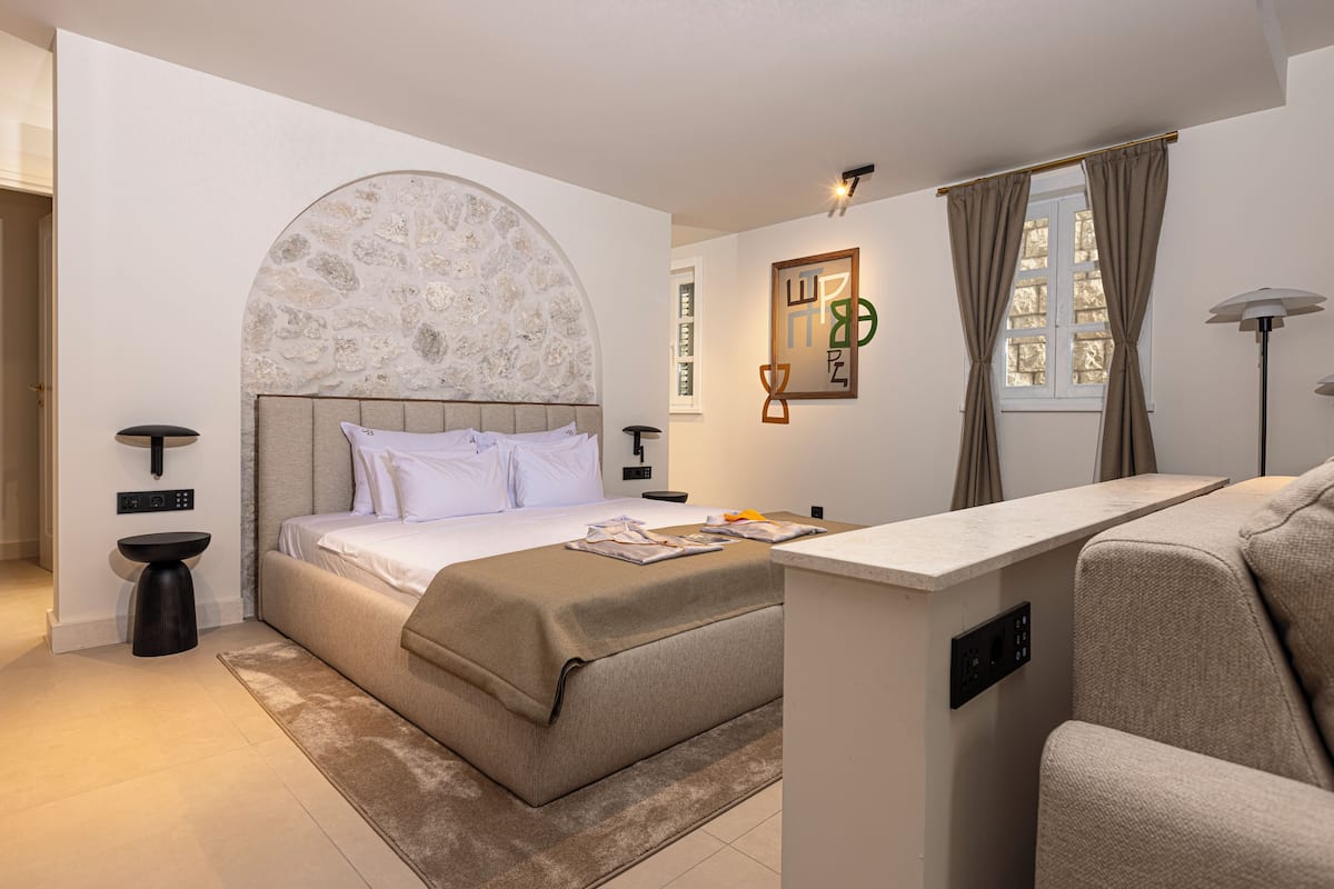 A modern bedroom with a large bed, a bedside table, a desk, and a window with curtains.