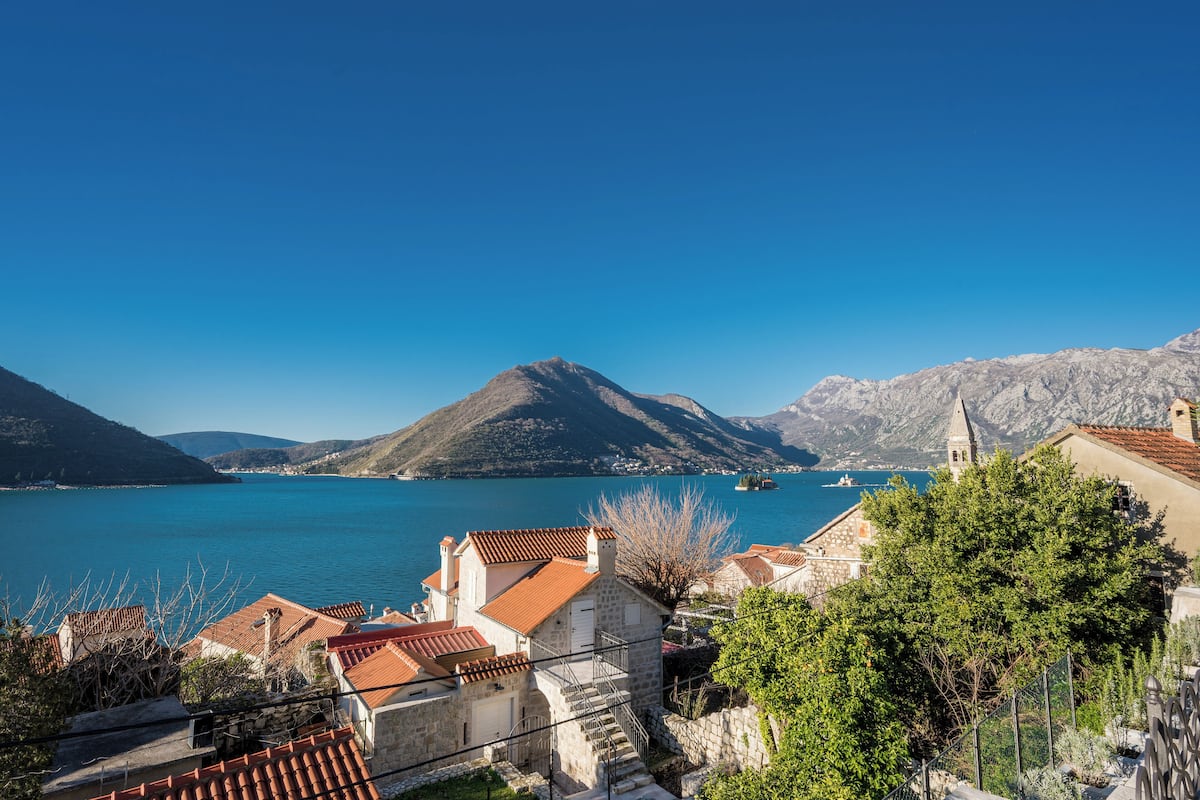A coastal town with stone buildings, a church, and a clear blue sea.
