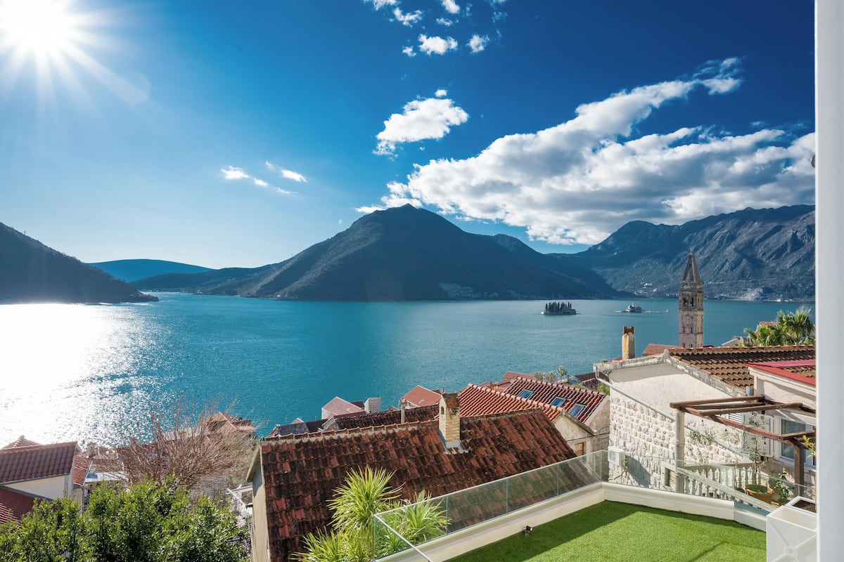 A coastal view with a mountain, a body of water, and a building with a red-tiled roof.