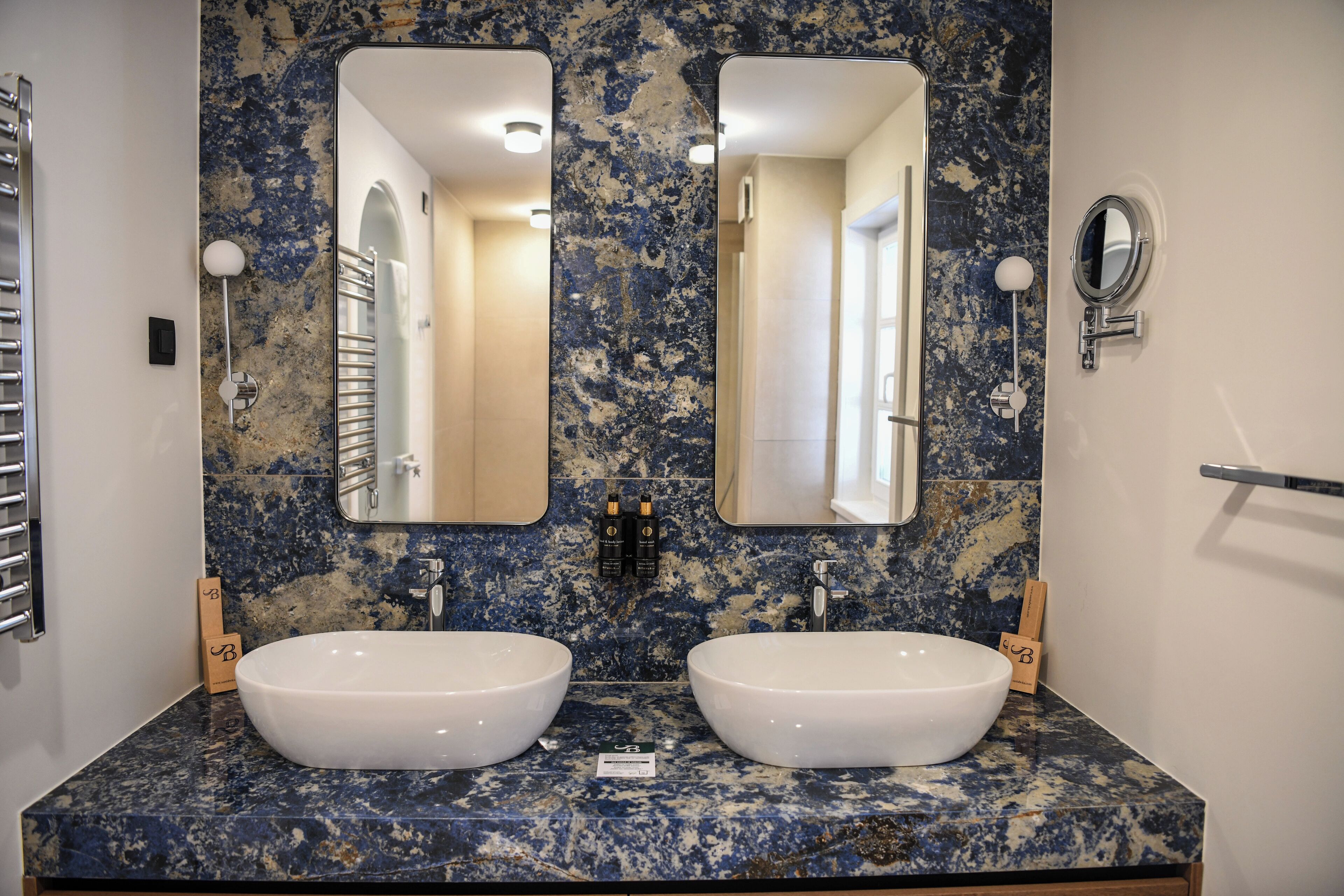 A bathroom with two sinks, marble backsplash, and large mirrors.