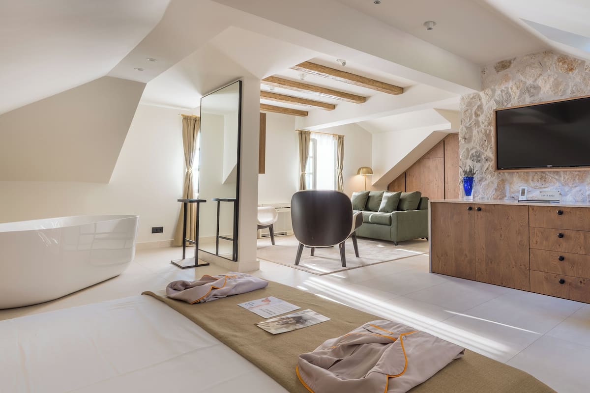 A modern, well-lit room with a large bathtub, a wooden ceiling, a flat-screen TV, and a stone wall.