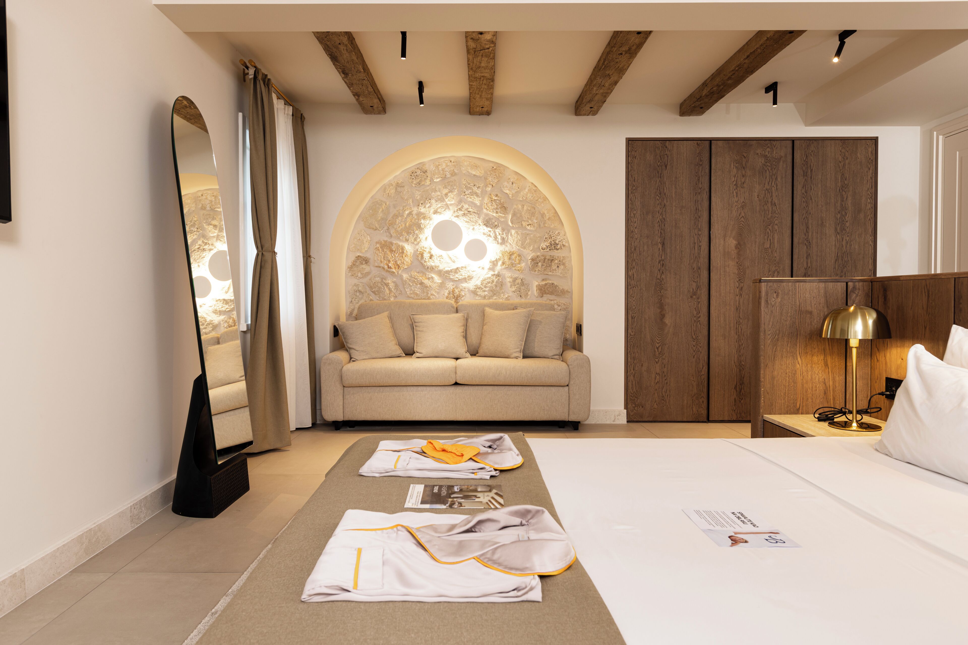 Habitación de hotel moderna con una cama grande, un sofá, un espejo y una pared de arco de piedra.