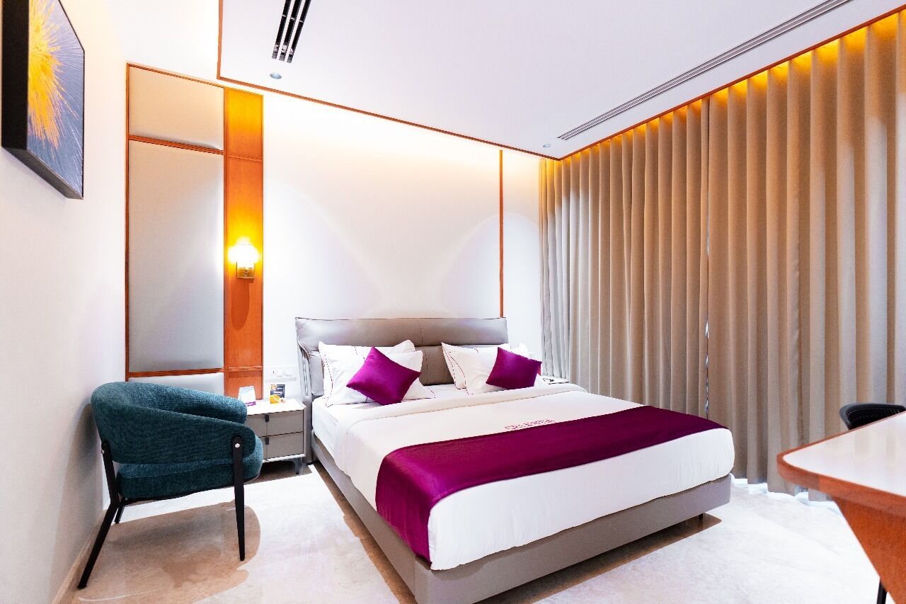 A modern hotel room with a large bed, a desk, and a chair.