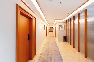 Un pasillo de hotel con puertas de madera, una alfombra estampada y una fila de ascensores.
