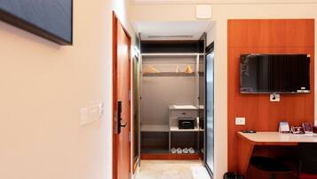 Habitación de hotel con escritorio de madera, televisor montado en la pared, armario con ropa colgada y zapatero.