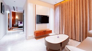 Ein modernes Hotelzimmer mit Flachbildfernseher, rundem Couchtisch, einer Sitzecke und einem großen Fenster mit Vorhängen.