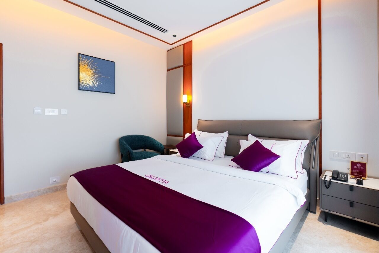 A hotel room with a large bed, a nightstand, a chair, a wall-mounted mirror, and a painting.