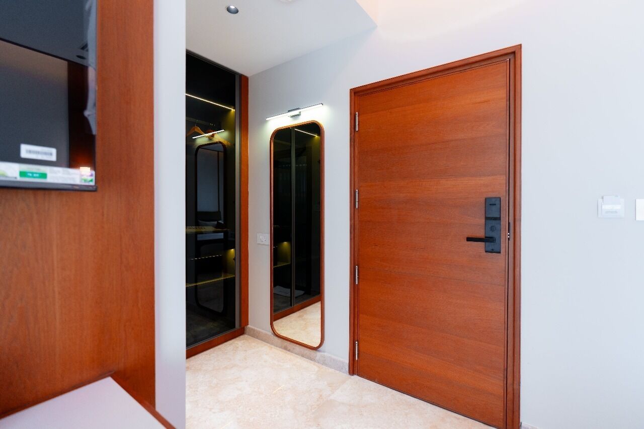 Un pasillo con una puerta de madera, un espejo y un estante con un dispositivo.