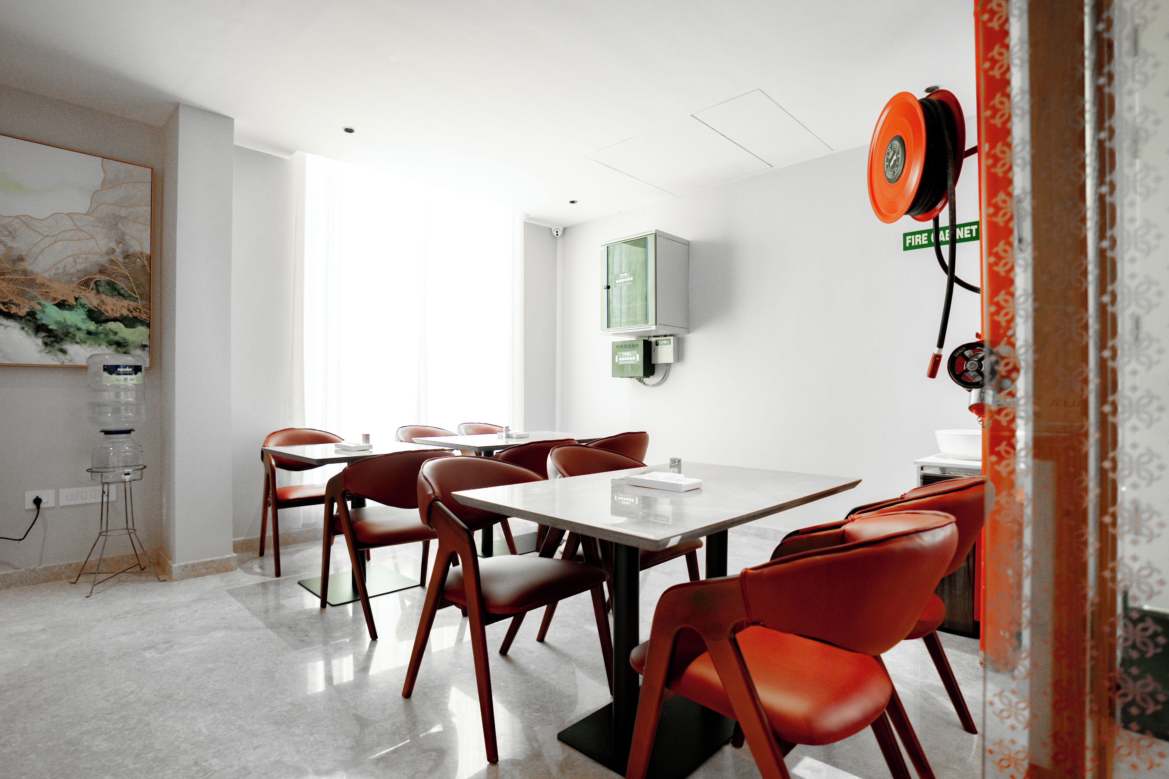 Un'area pranzo moderna con un tavolo bianco e sedie rosse, un distributore d'acqua e un rilevatore di fumo a parete.