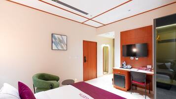 Habitación de hotel con cama, escritorio, silla, televisor y espejo.