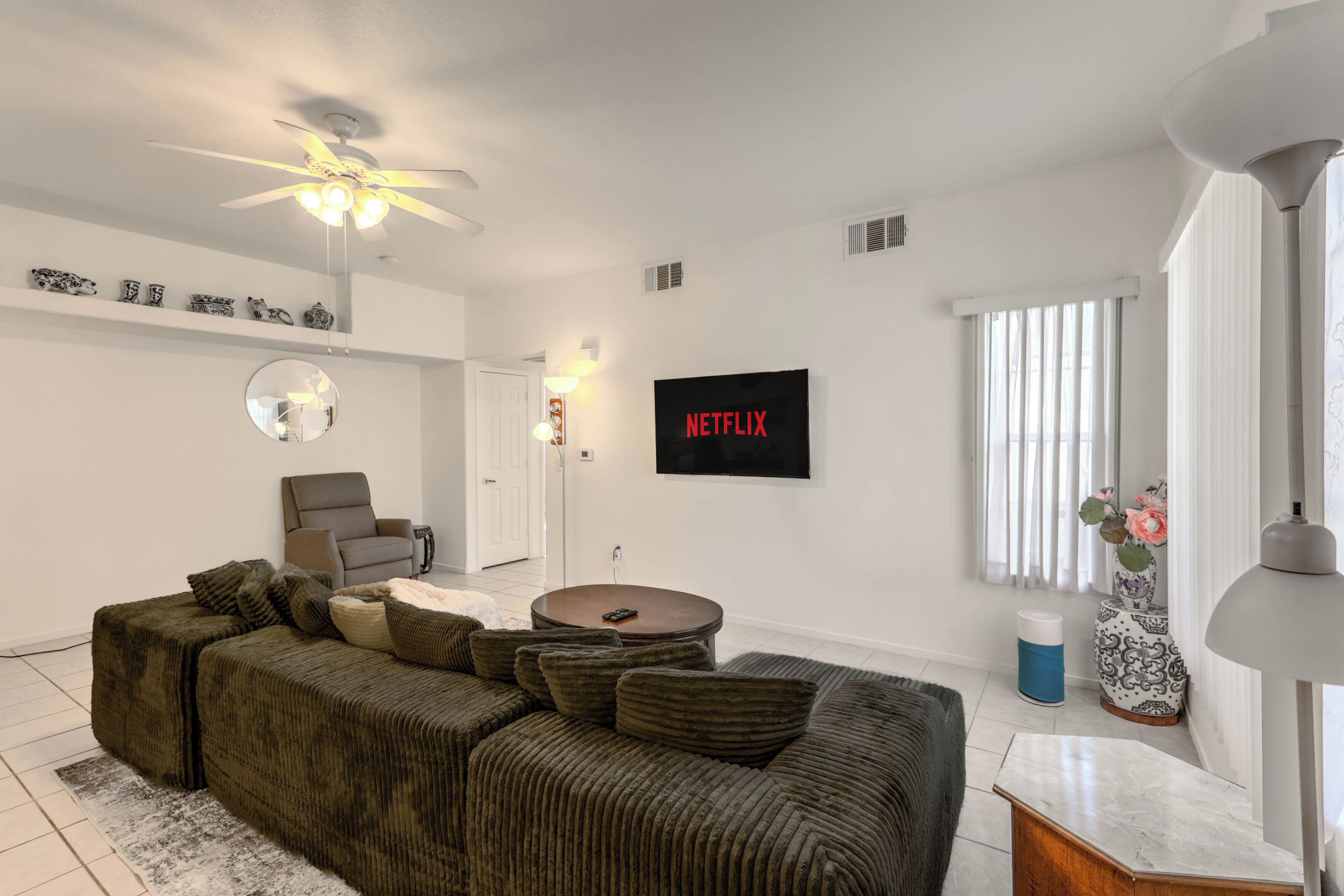 Uma sala de estar moderna com sofá seccional, ventilador de teto, TV na parede e janela com persianas.