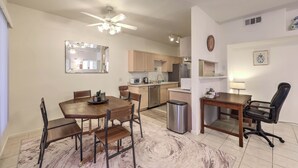 Une cuisine moderne avec des meubles en bois, un coin repas avec une table et des chaises en bois, une petite poubelle et un ventilateur de plafond.
