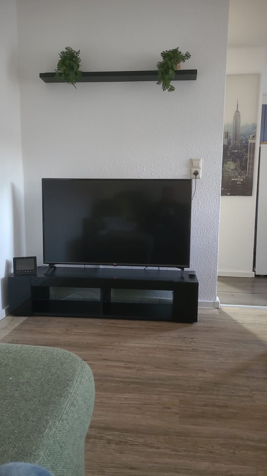 A living room with a large flat-screen TV on a black stand, a small table with a device, and a green chair.