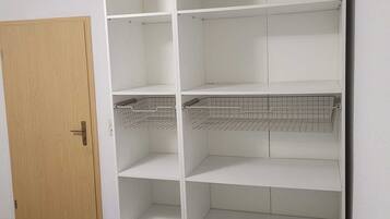 A room with a wooden door, white shelving unit with wire baskets, and a bed with a blue and white striped blanket.
