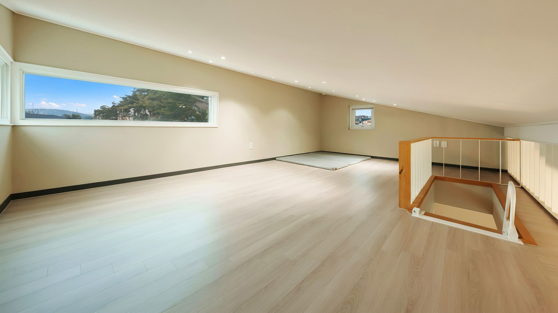 A spacious room with a large window, a wooden floor, and a built-in bench.