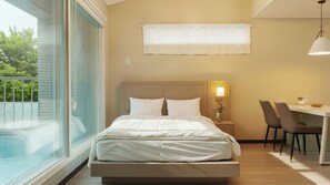 Habitación de hotel moderna con una cama grande, un escritorio con sillas, una lámpara y vistas a zonas verdes.