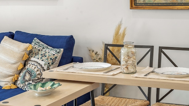 Un comedor con una mesa para dos, un sofá azul y cojines decorativos.