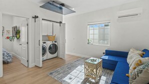 Una sala moderna con un sofá azul, una lavadora y un ventanal grande.