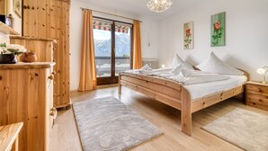 Un dormitorio con cama de madera, cómoda, mesita de noche y vistas a montañas a través de un ventanal grande.