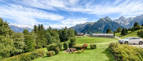 A scenic view of a mountainous landscape with a well-maintained lawn, a small building, and a parked car.