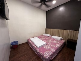 Quarto com cama, ventoinha no teto, televisão fixada na parede e uma pequena lixeira.