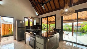 Une cuisine moderne dotée d’un îlot central, d’appareils électroménagers en acier inoxydable et de grandes fenêtres donnant sur un jardin.