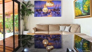 Un salon avec un canapé, un grand tableau représentant des bateaux, un luminaire suspendu et une plante en pot.