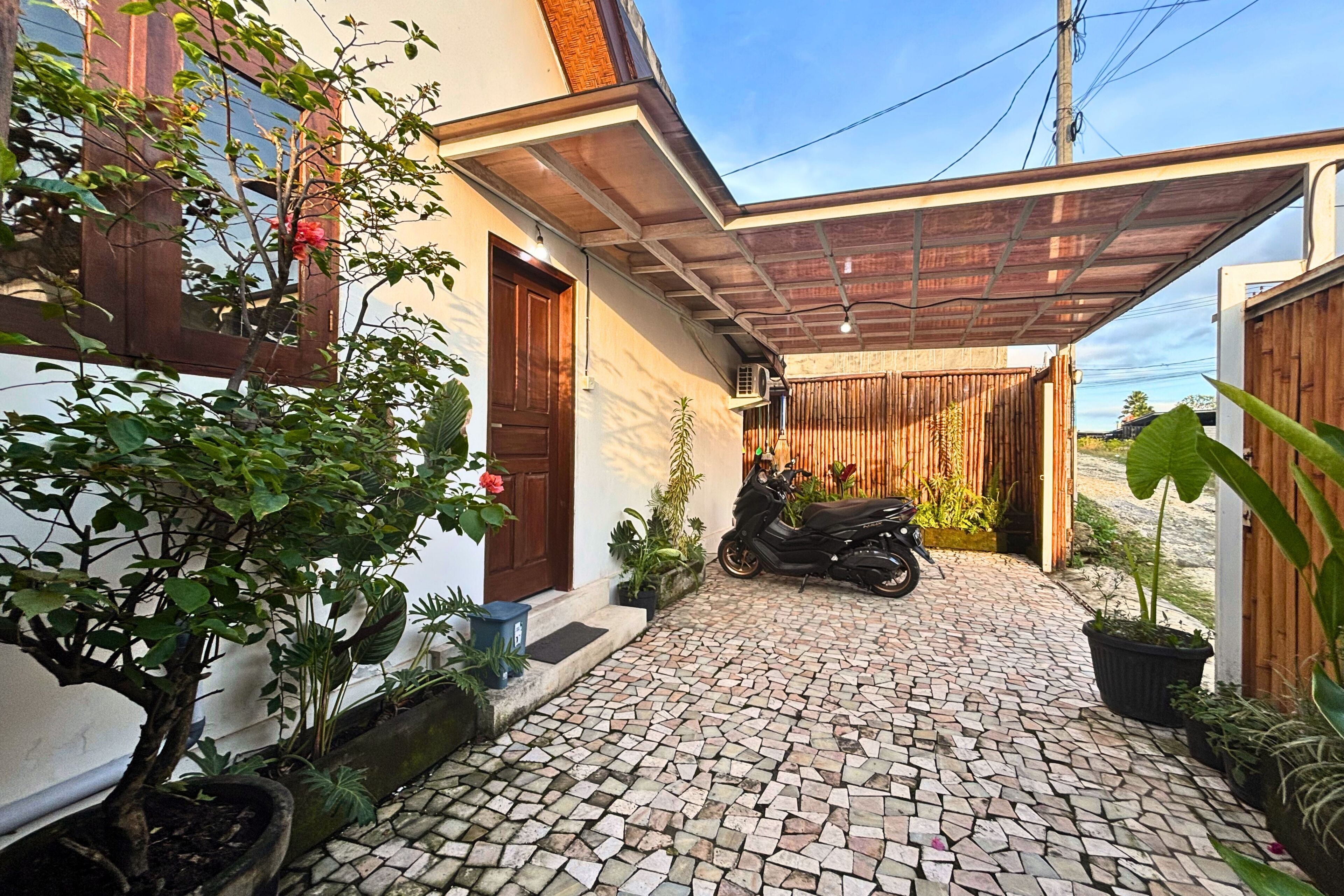 A paved courtyard with a motorcycle, potted plants, and a wooden gate.