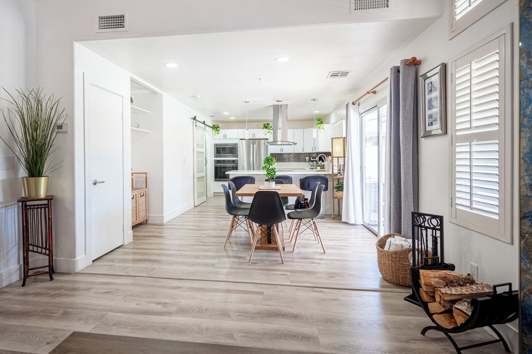 Une cuisine moderne avec des meubles blancs, un îlot central et un coin repas comprenant une table et des chaises en bois.