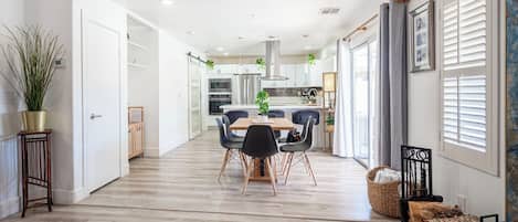 A modern kitchen with white cabinets, a central island, and a dining area with a wooden table and chairs.