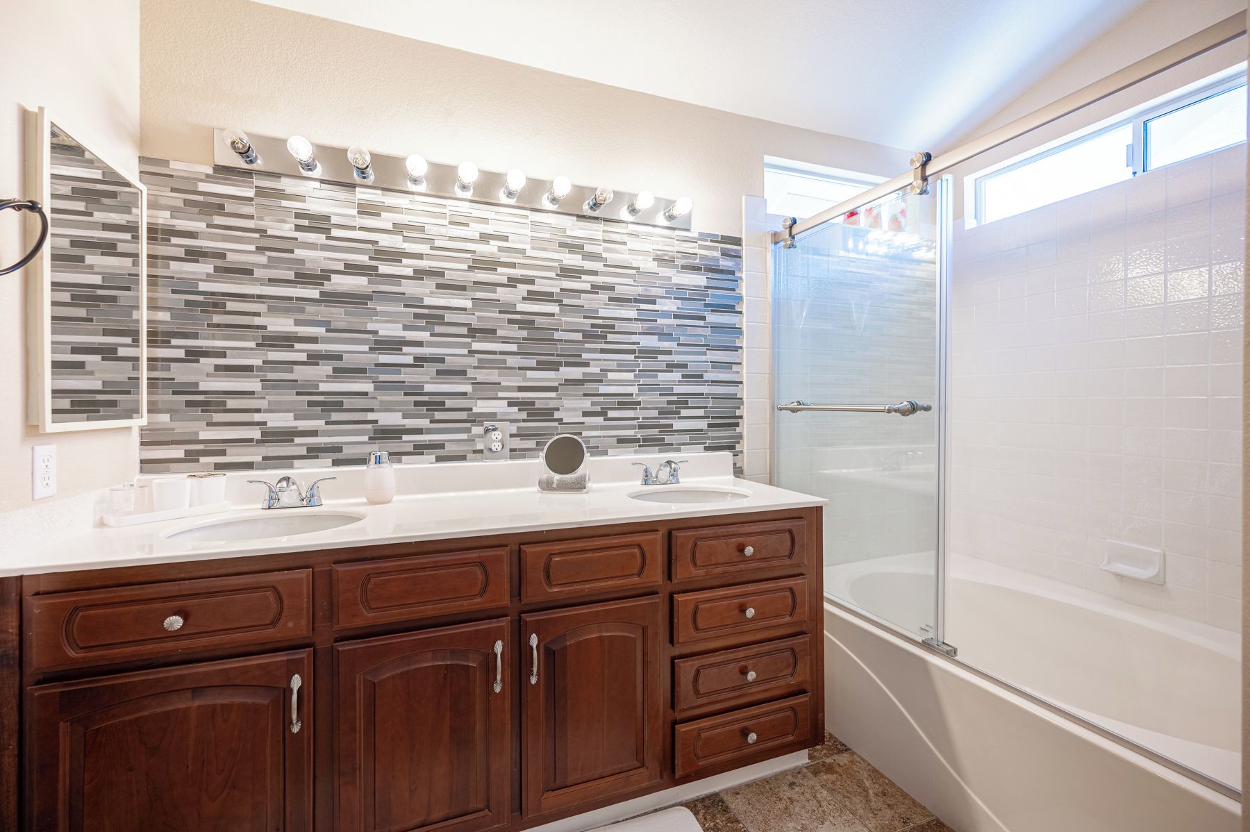 A bathroom with a double sink vanity, a mirror, a tiled backsplash, and a glass shower enclosure.