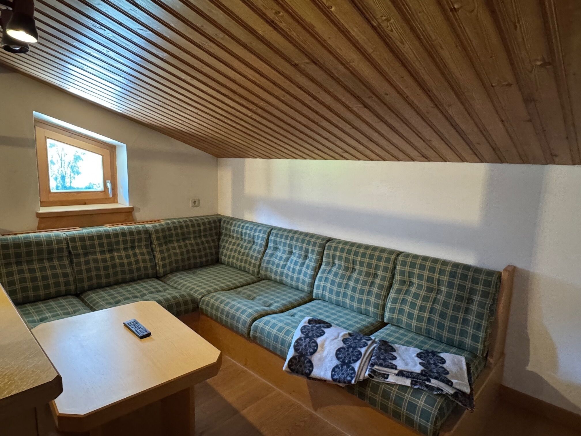 A cozy room with a green plaid sofa, a wooden table, and a window with a view.