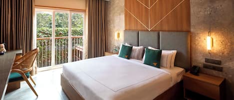 Habitación de hotel con una cama grande, un escritorio y una silla. Tiene un balcón con vistas a zonas verdes.