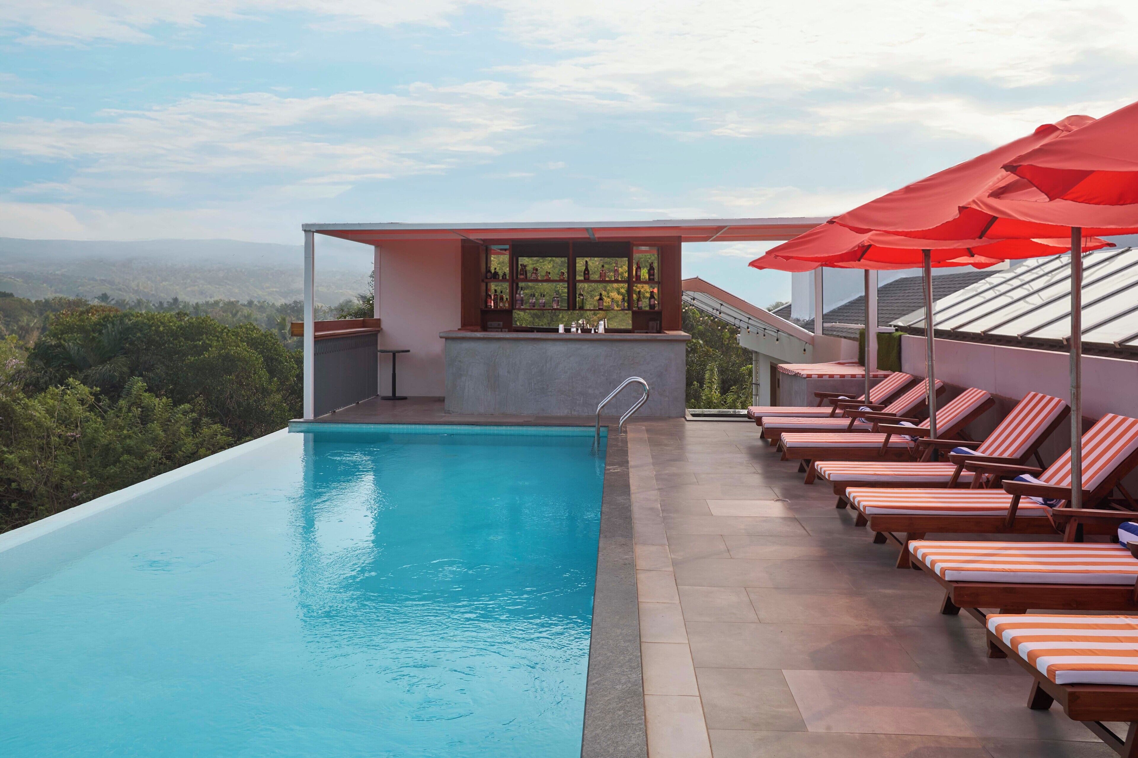 A rooftop infinity pool with lounge chairs and umbrellas, a bar, and a view of the landscape.