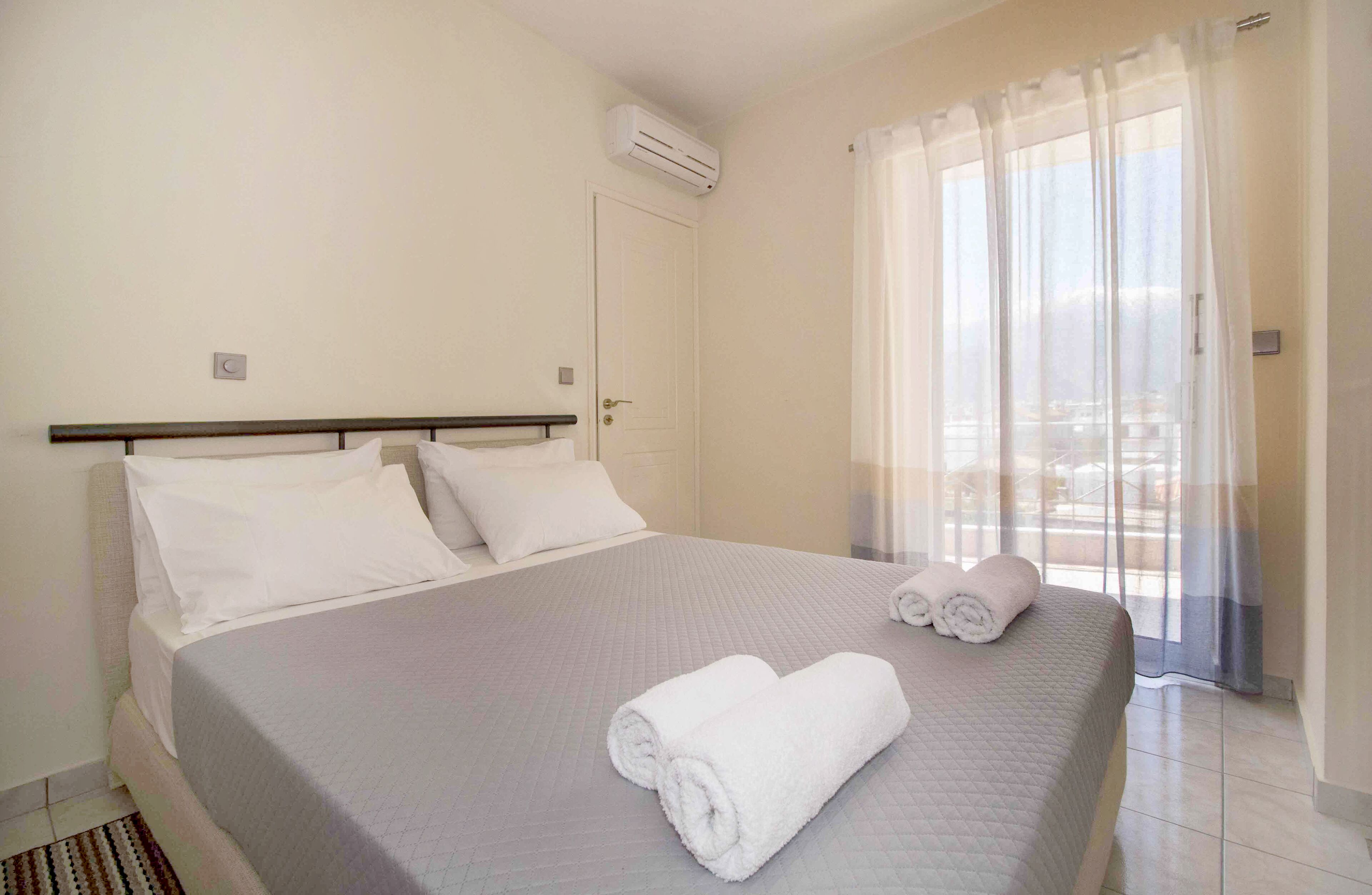 A hotel room with a bed, a window with sheer curtains, and an air conditioning unit on the wall.
