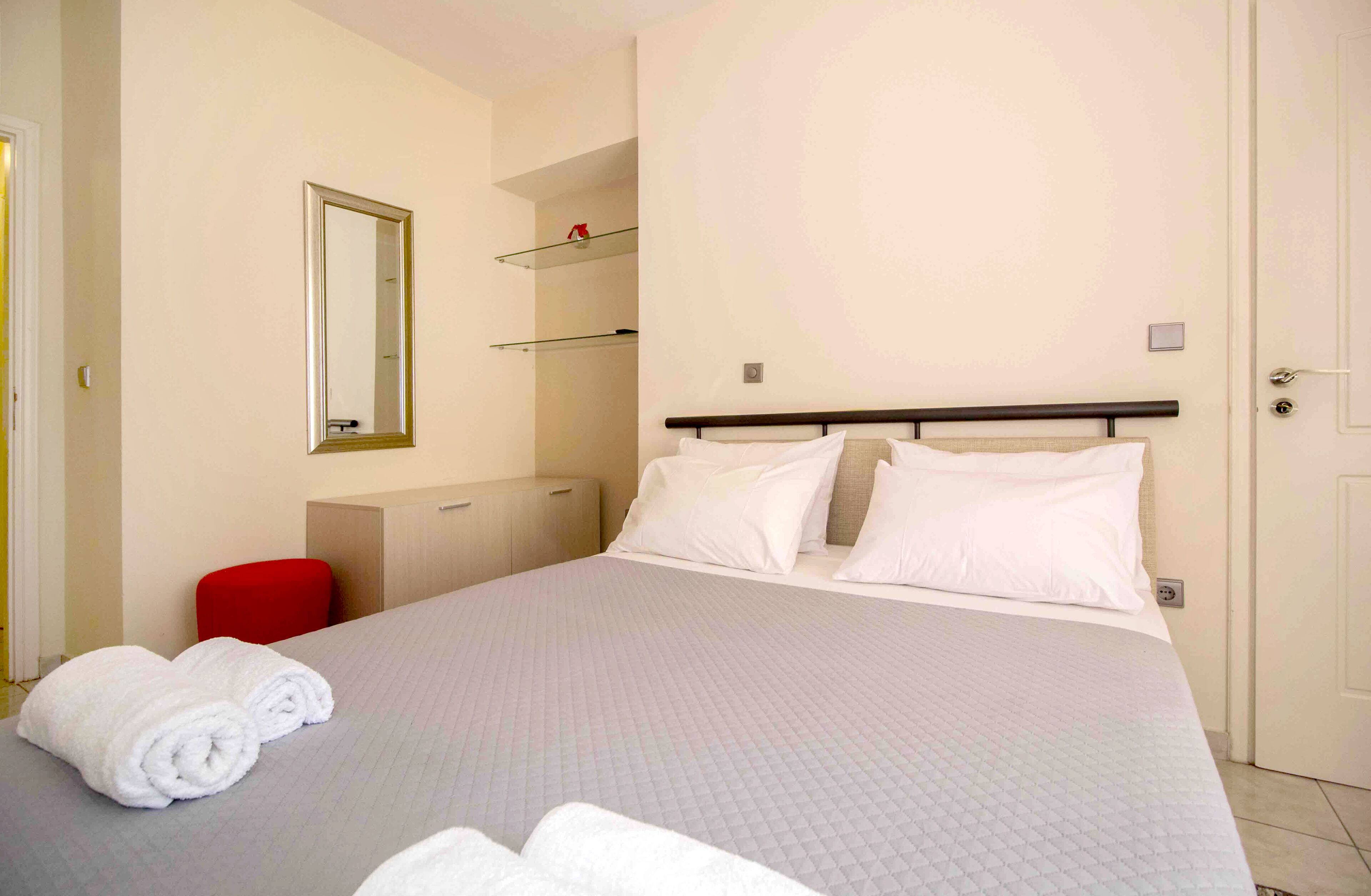 A hotel room with a large bed, a red chair, a mirror, and a wardrobe.