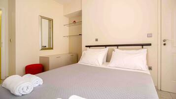 A hotel room with a large bed, a red chair, a mirror, and a wardrobe.